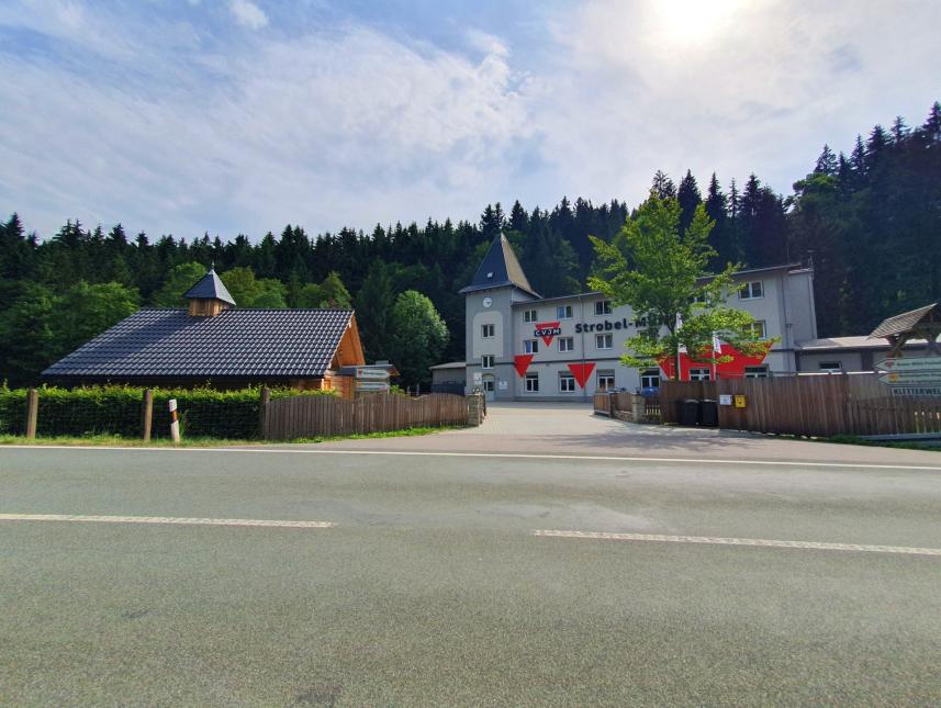 Bild mit Zufahrt, Blick aufs Gruppenhaus und linker Hand kuckt das Dach der Blockhauskapelle über der Hecke heraus
