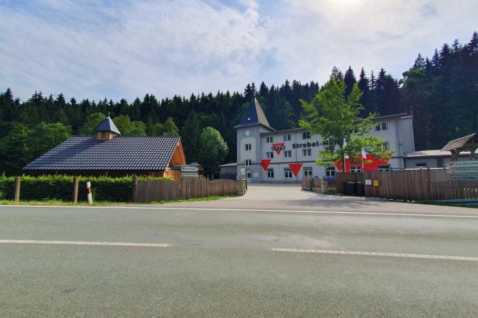 Bild mit Zufahrt, Blick aufs Gruppenhaus und linker Hand kuckt das Dach der Blockhauskapelle über der Hecke heraus