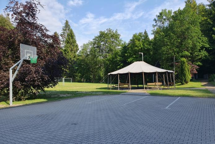Hof mit Blick zum Streetballkorb, Spielwiese mit Fußballtoren und der Lagerfeuerstelle mit Jurtendach