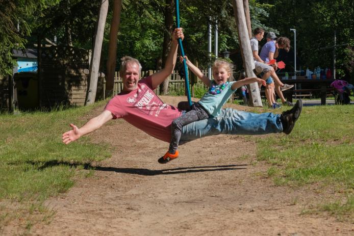 Vater und Tochter fahren Seilbahn und stecken freudig die freie Hand in die Höhe