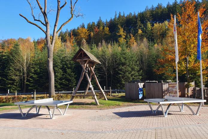 zwei Tischtennisplatten warten auf dem Freigelände auf Spieler; die Gastfreundefahne und die Fahne mit dem Logo der himmlischen Herbergen hängen mangels Wind schlaff am Mast