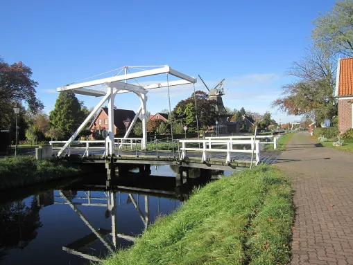 Weiße Klappbrücke über den Fehnkanal. Im Hintergrund die markante Windmühle.