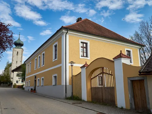 Das historische Pfarrheim von Kellberg, dahinter der Turm der Pfarrkirche St. Blasius.